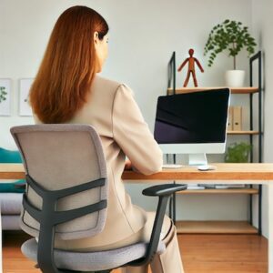 Female office worker sitting at her desk, facing her computer monitor, in a modern office setting with greenery in the background.