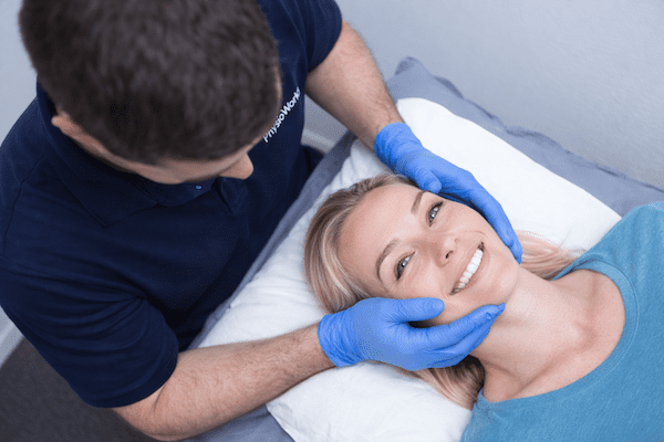 tmj-treatment-physiotherapy-jaw-pain-female-patient TMJ treatment physiotherapy with jaw support for female patient during clinic assessment