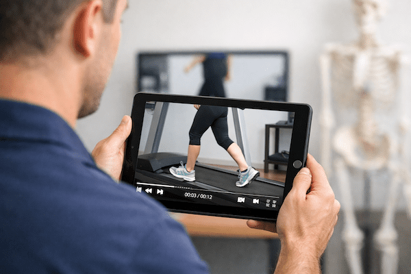 Physiotherapist reviewing side-view walking gait analysis on tablet assessing lower limb biomechanics