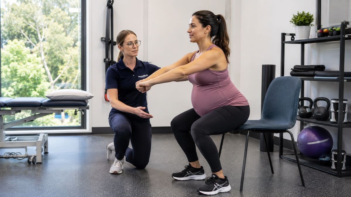 Pregnant woman performing a supported chair squat with physiotherapist guidance
