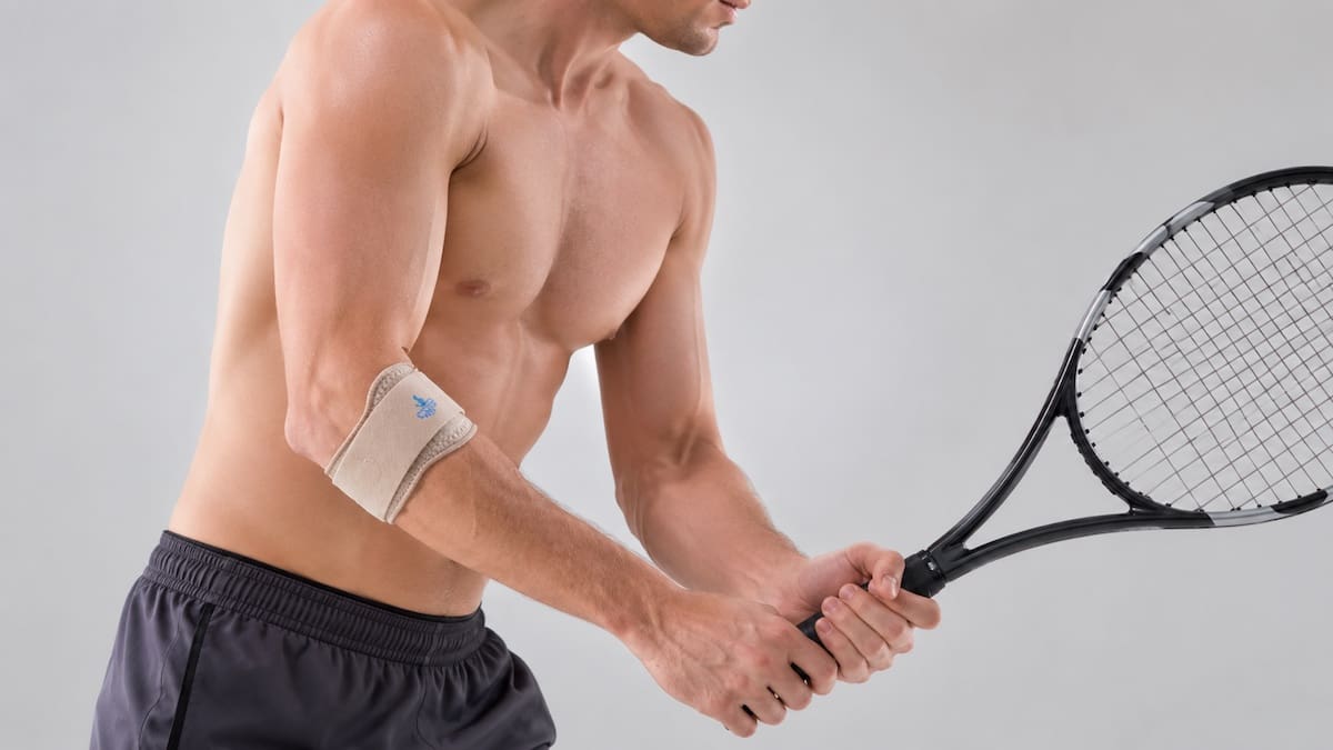 Tennis elbow brace positioned on the upper forearm while holding a tennis racquet