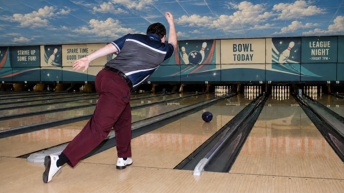 Ten pin bowler completing the slide and ball release down an indoor bowling lane